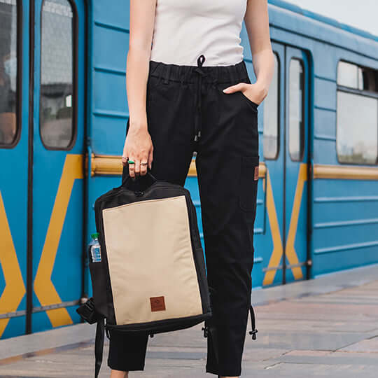 Woman in black pants and the beige backpack in her hand