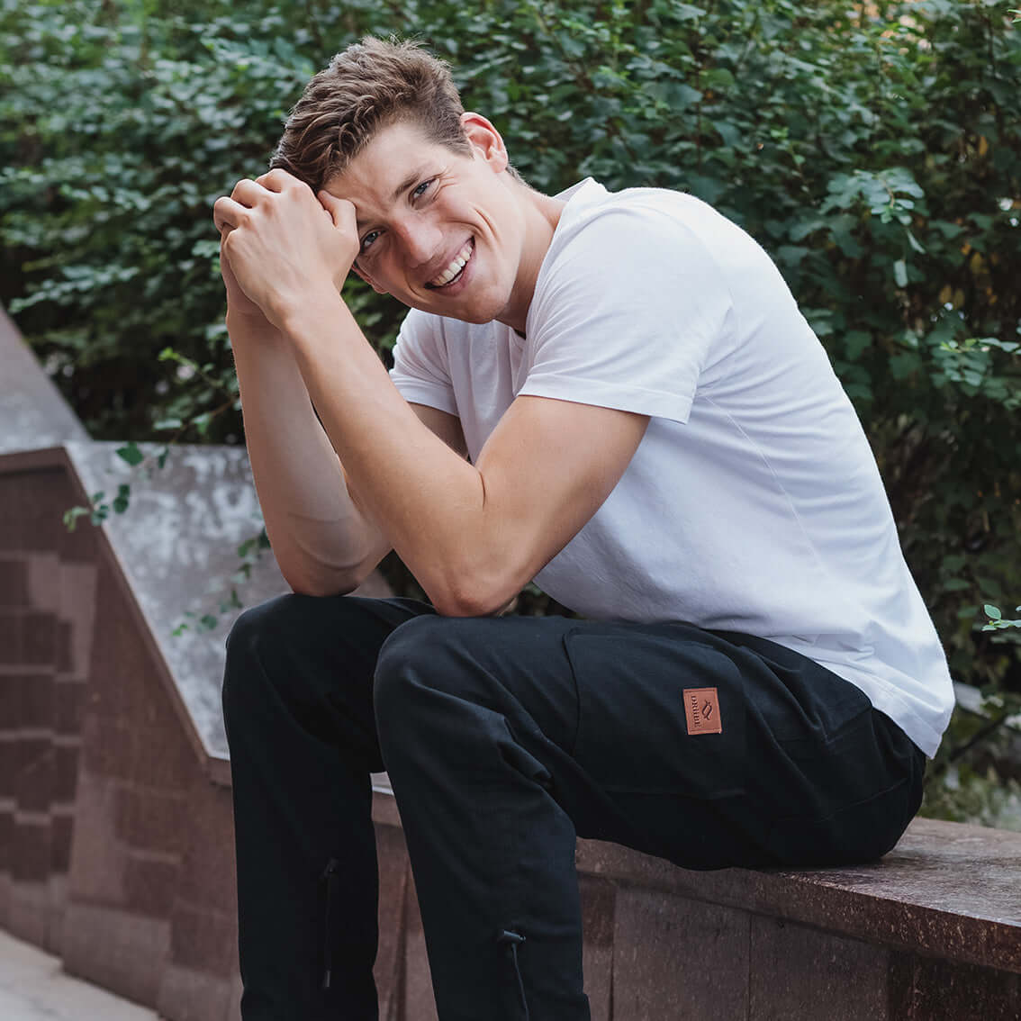 Smiling man sitting in the park wearing pants with DRiiBE label