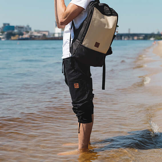 Man near the river wears pants with shortened length and backpack over his shoulder