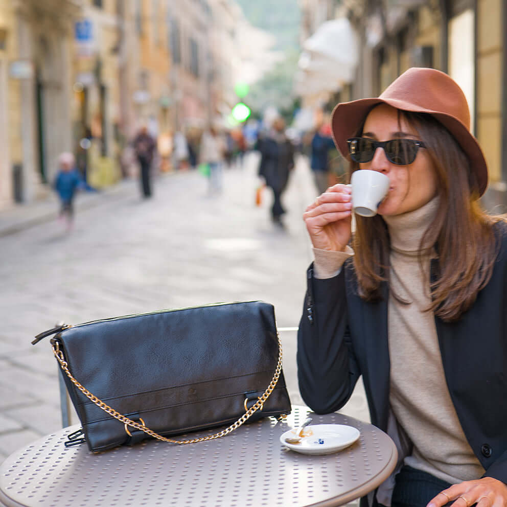 The woman is drinking coffee with her DAKOTA black convertible bag on the table